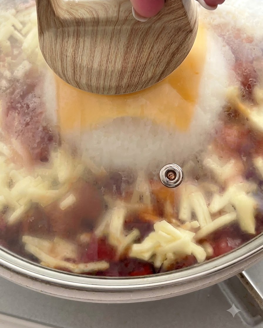 溶けるチーズとご飯の上に閉じ込められた蒸気がガラス蓋の内側に見える、蓋をしたフライパン。