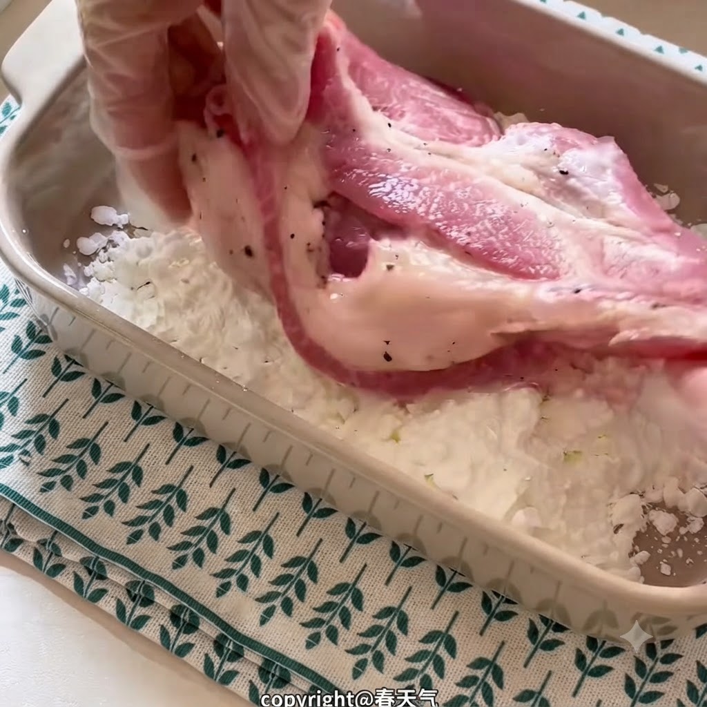 手袋をした手で下味をつけた豚肉を持ち、長方形の陶器の皿の中で片栗粉をまぶしている。