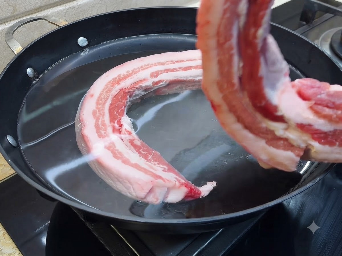 冷水の入った大きな鍋に入れられる生肉の豚バラ肉。