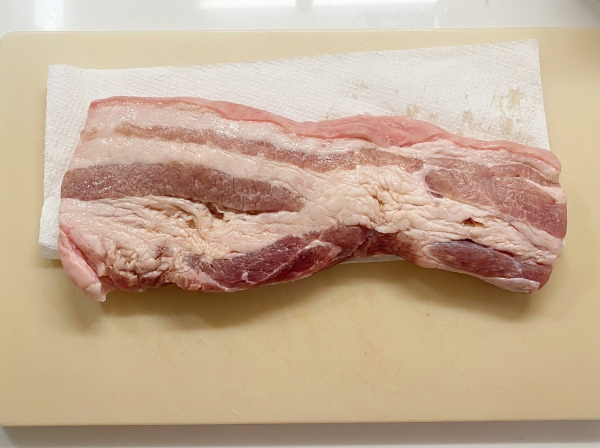まな板の上のペーパータオルの上に平らに置かれて乾燥されている豚バラ肉の細切り。