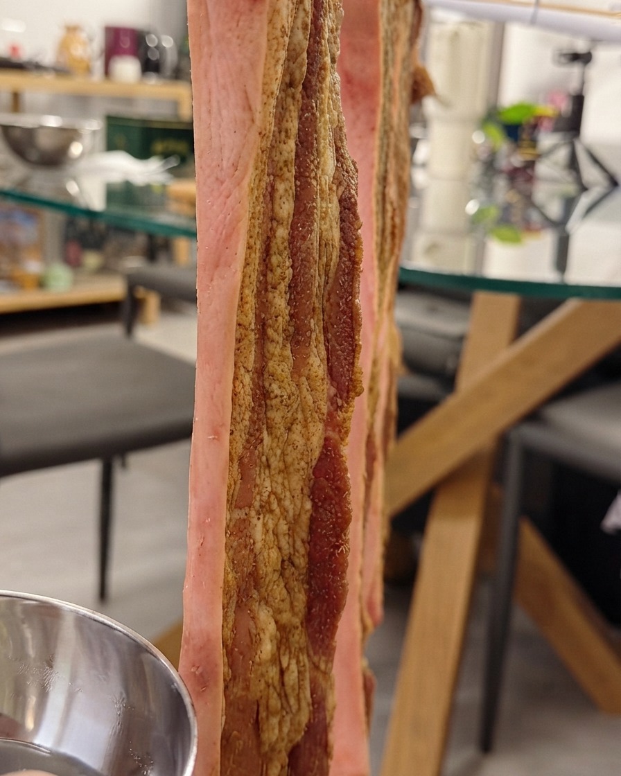 ラックに垂直に吊るされ、皮にカリカリにする水を刷毛で塗られている豚バラ肉。