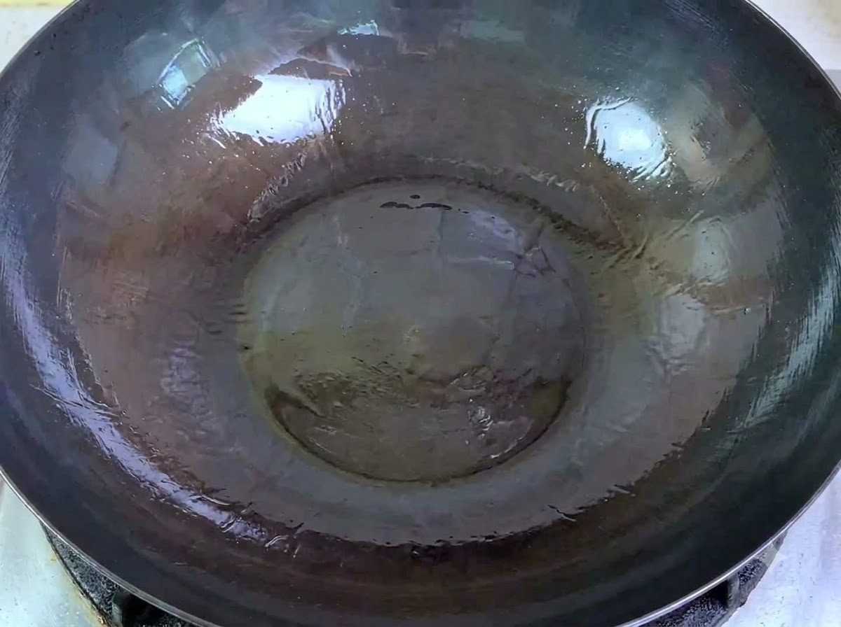 生の一口大の豚ひき肉を、熱した油が入った大きめの中華鍋にボウルから流し込んでいるところ。