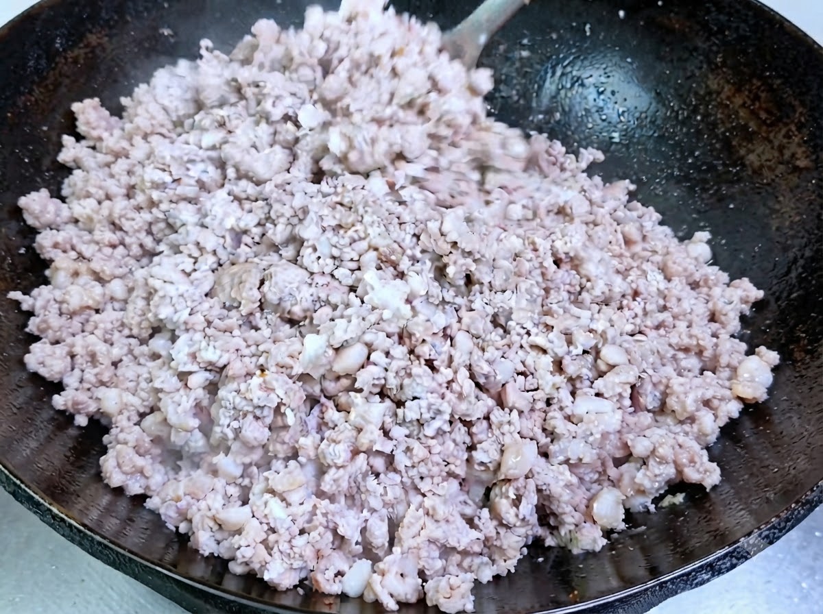 味付けされた中華鍋の中で、ひき肉に火が通り不透明に変わりながら炒められているところ。
