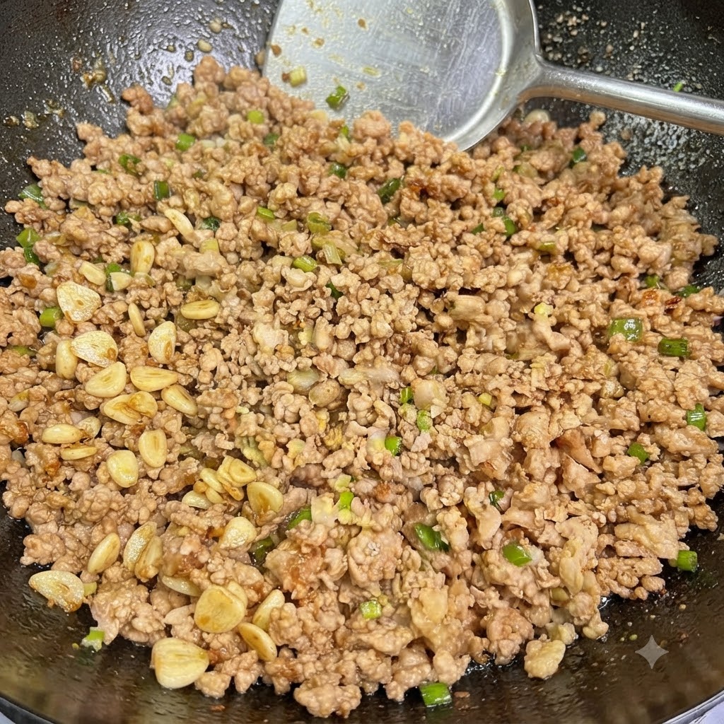 炒めた豚ひき肉に長ねぎとにんにくを加え、中華鍋の中でヘラを使って混ぜ合わせているところ。