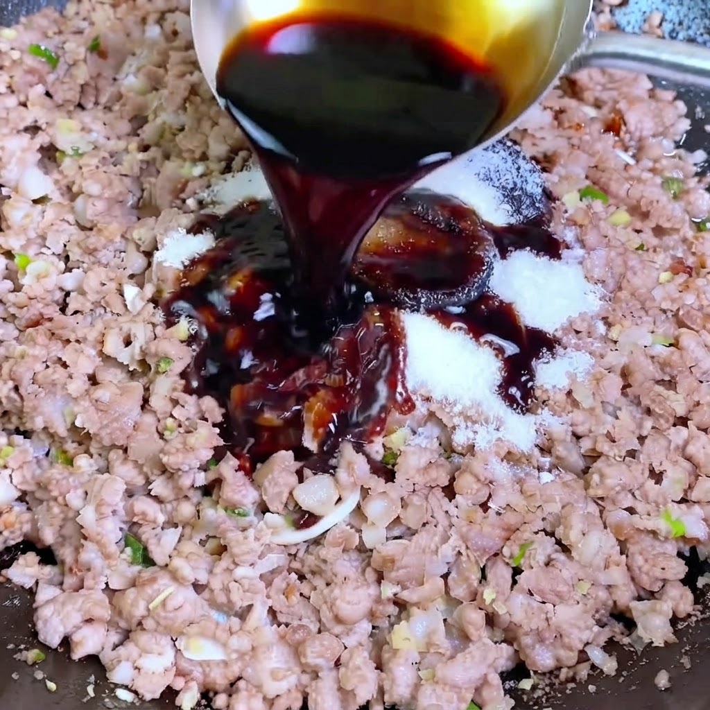 銀色のおたまから、ひき肉と白い調味料が入った中華鍋へとダークソイソースが注がれているところ。