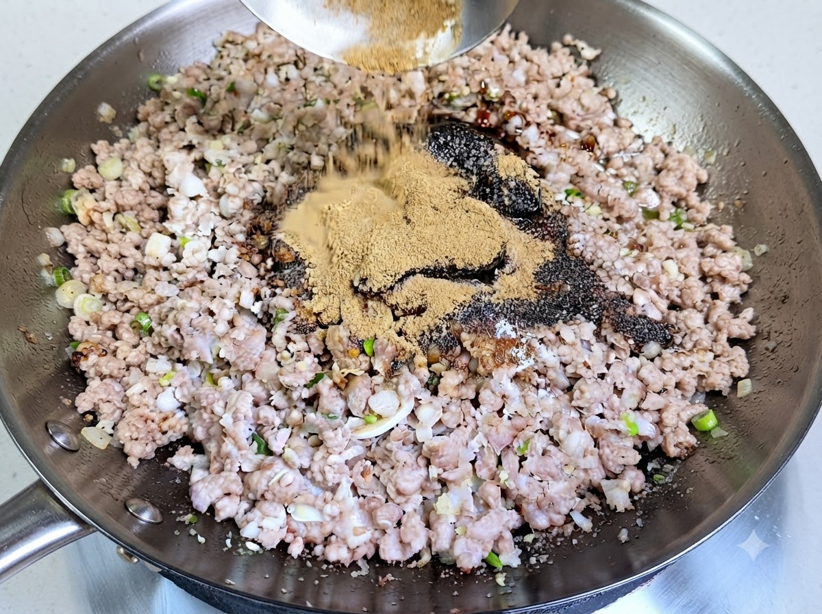 味付けされたひき肉の上へ、おたまから薄茶色のスパイスパウダーがたっぷりとかけられているところ。