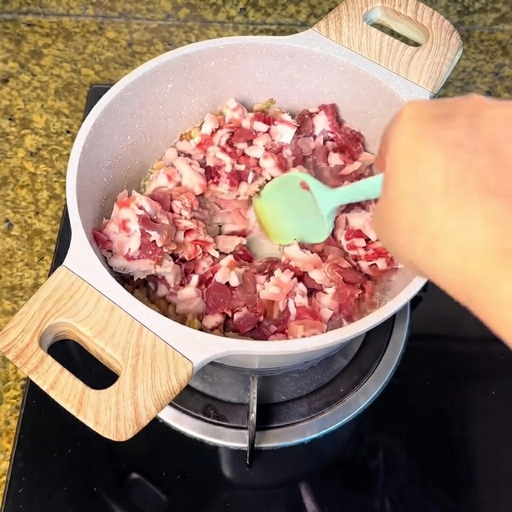 溶け出した脂の入った鍋に豚肉の細切れが投入され、緑色のシリコンスパチュラで混ぜ合わされている様子