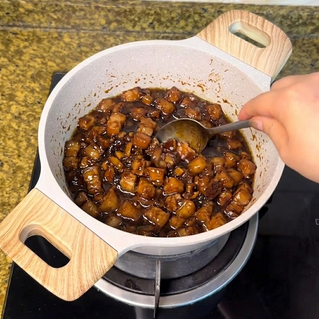 煮立っている濃い色の肉味噌に、スプーンで白砂糖が加えられて混ぜられている様子