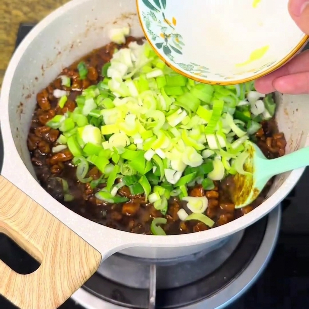 ボウルから刻み青ねぎが泡立つ肉味噌の中に投入されている様子
