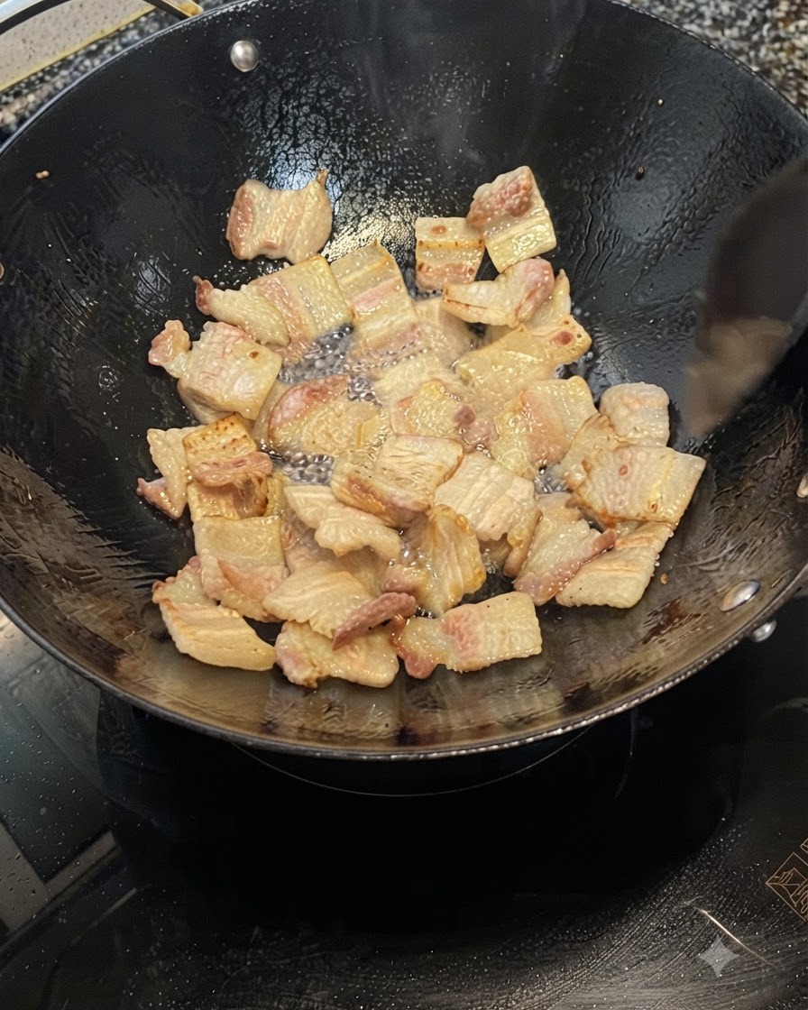 中華鍋の中で豚バラ肉のスライスが脂を出しながらきつね色に揚げ焼きにされている様子。