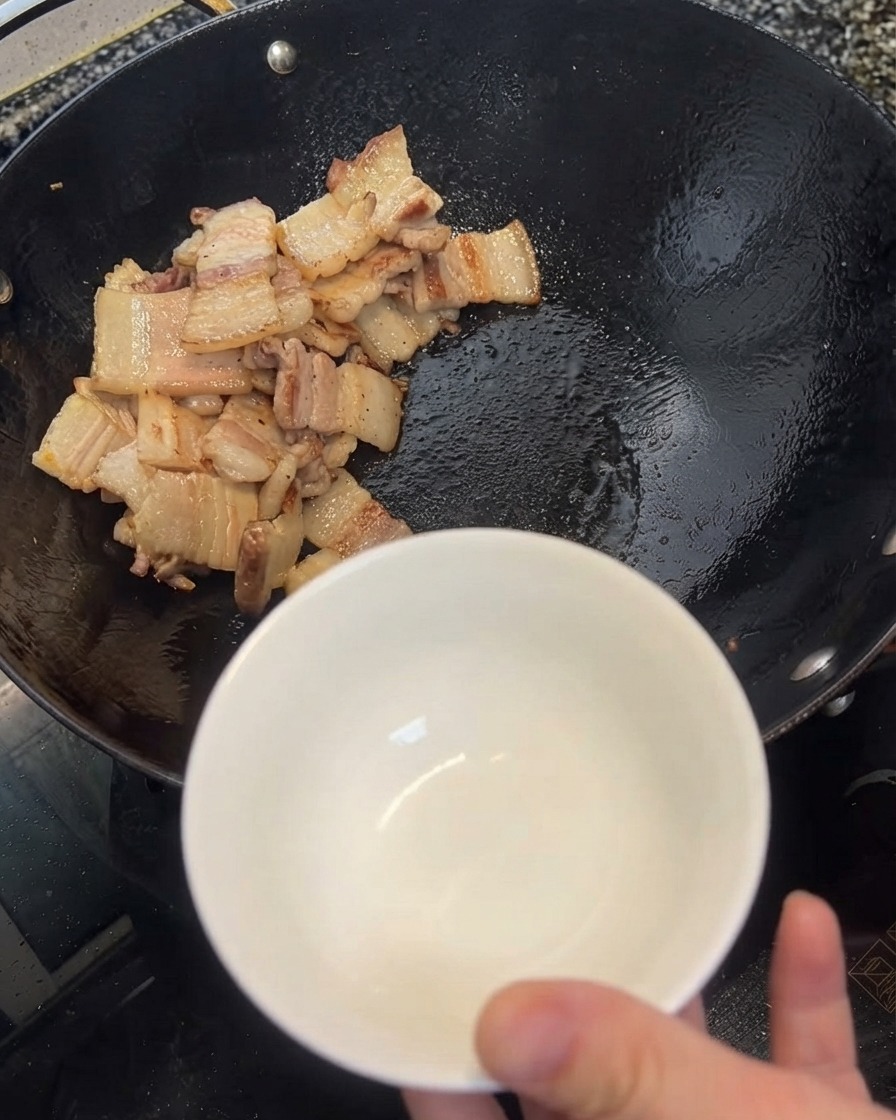 ヘラを使って中華鍋から余分な油を白いボウルにすくい取っている様子。