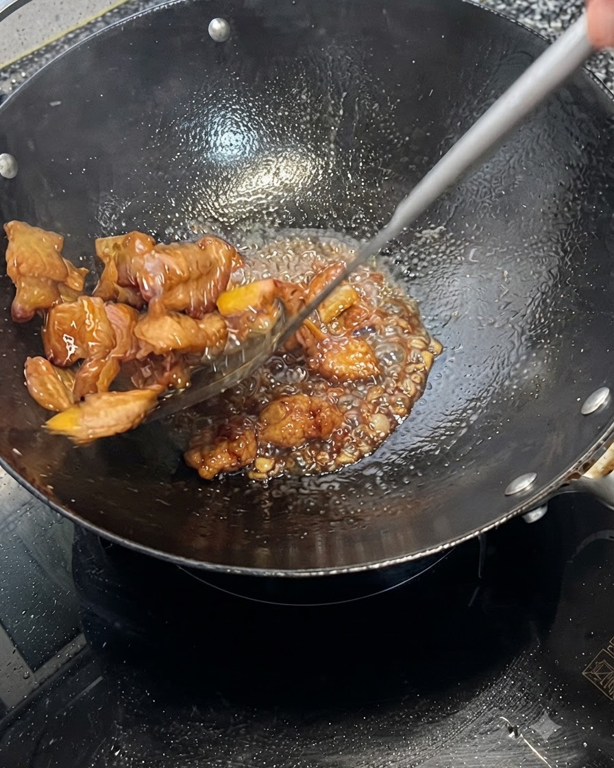 中華鍋の中で豚バラ肉が泡立つ濃い色のタレに素早く和えられている様子。