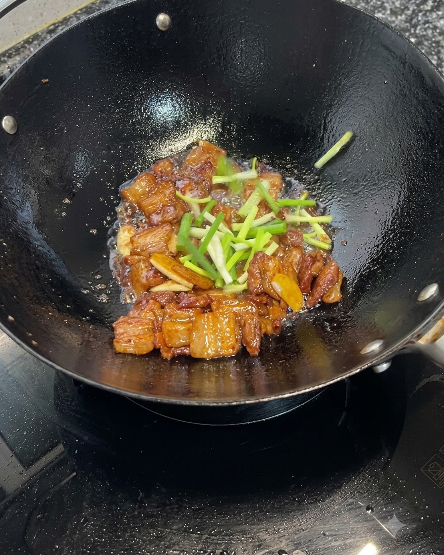 中華鍋で煮詰められキャラメリゼされた豚バラ肉の上に、新鮮な青ネギの小口切りが散らされている様子。