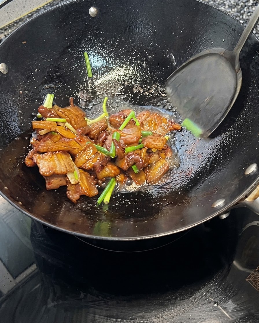 熱い中華鍋の中でヘラを使い、豚バラ肉と青ネギを一緒に炒め合わせている様子。