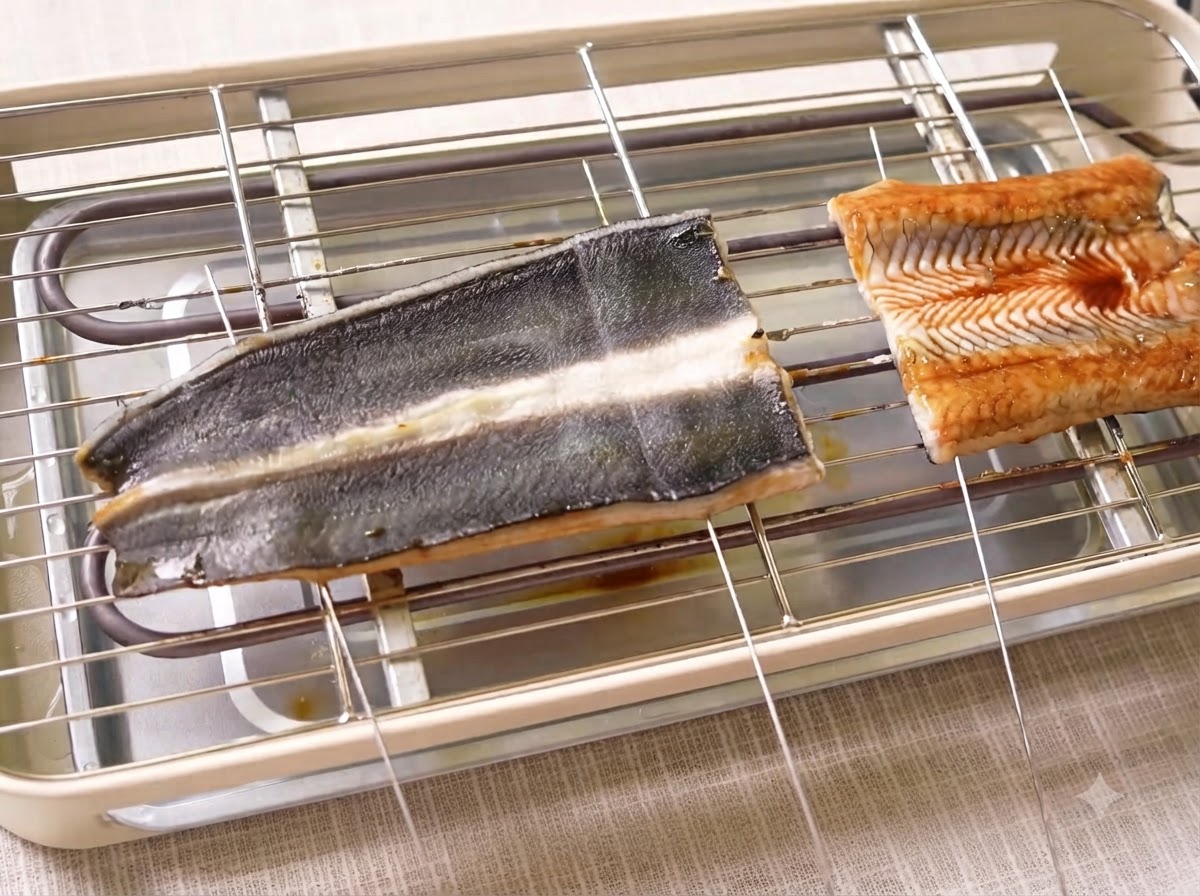 金属の串が肉に刺さった状態で、電気グリル上で調理されているうなぎの切り身。