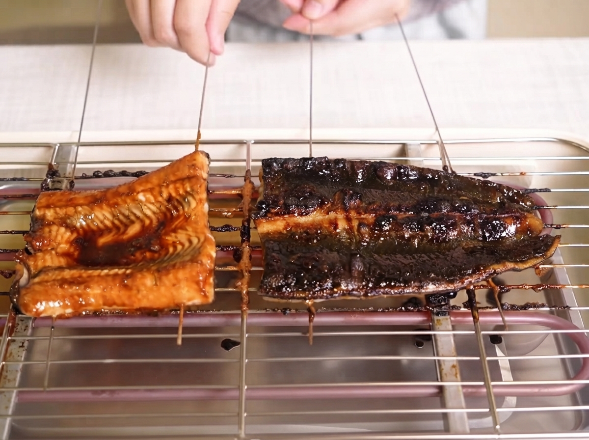 グリルラックの上で、焼き色がついてきたうなぎの切り身にツヤのある黒いタレが塗られている様子。