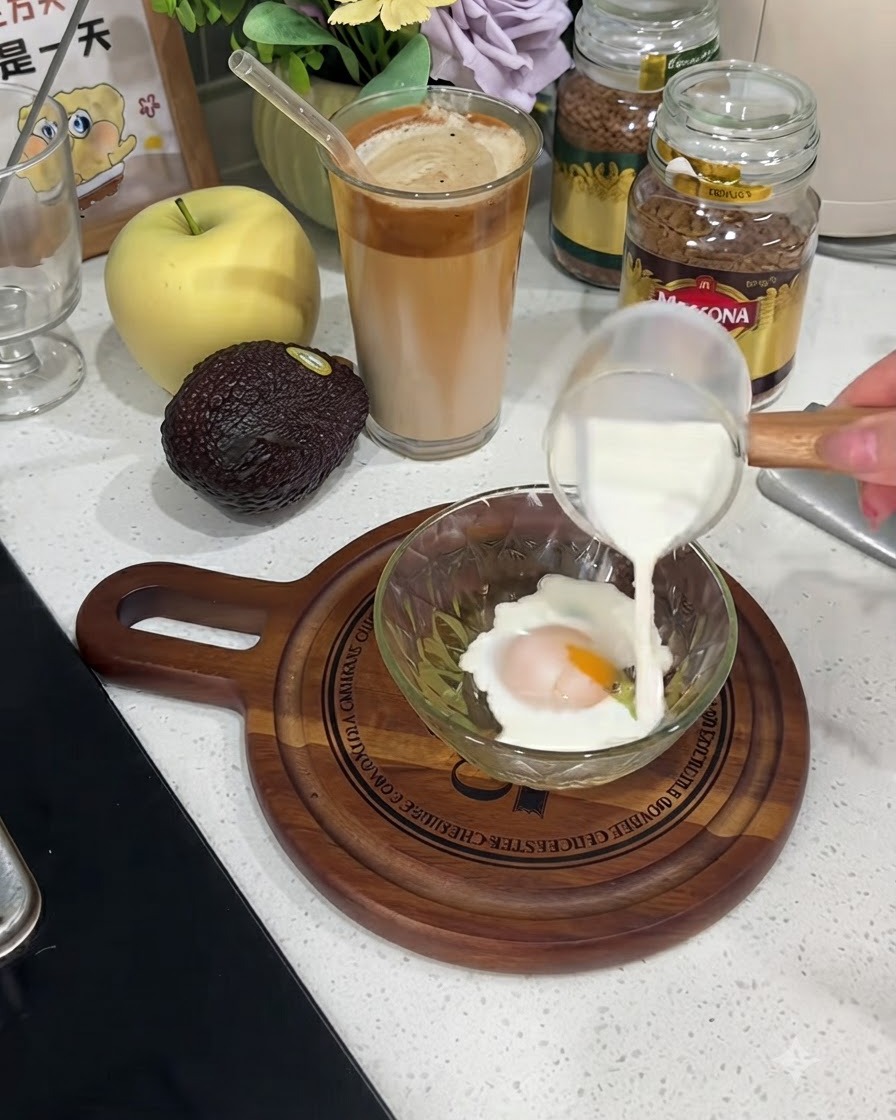 小さなガラスのピッチャーから、割った卵が入ったボウルに牛乳が注がれている様子。