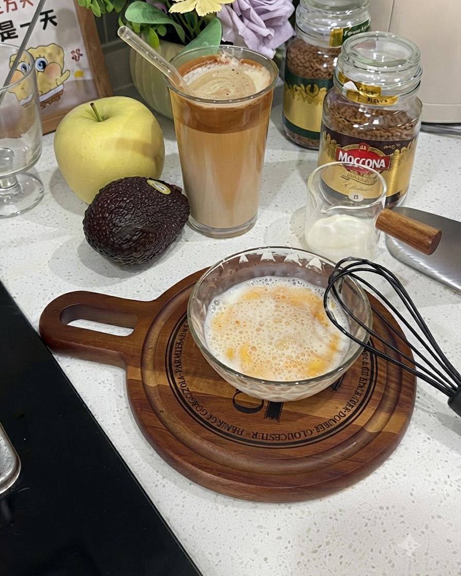 黒い泡立て器の隣に置かれた、泡立った卵と牛乳の混合液が入ったガラスボウル。