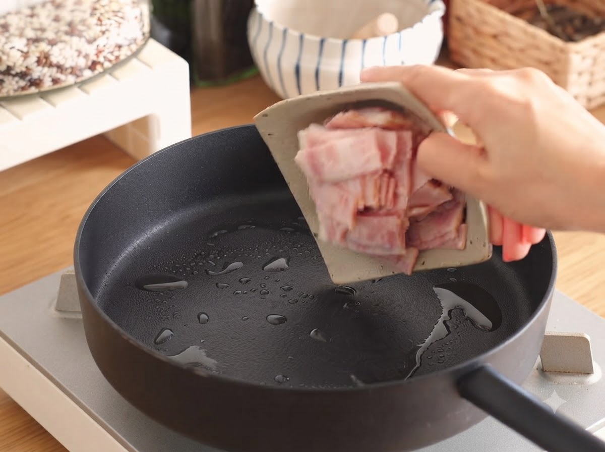 少量の油とともにフライパンの中でジューシーに焼かれているベーコンの細切り。