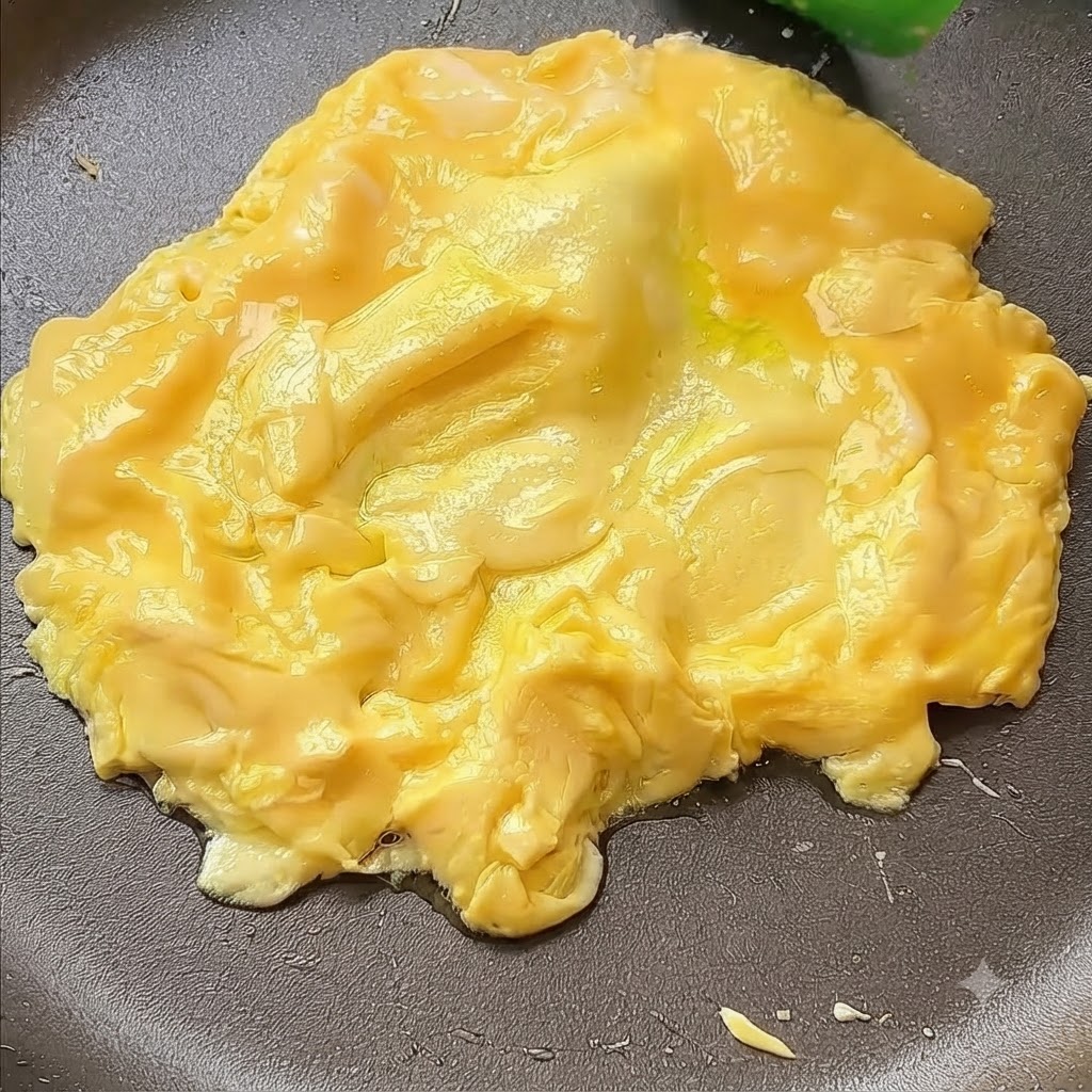 スパチュラを使って卵をフライパンの中央へと寄せ集めている様子。