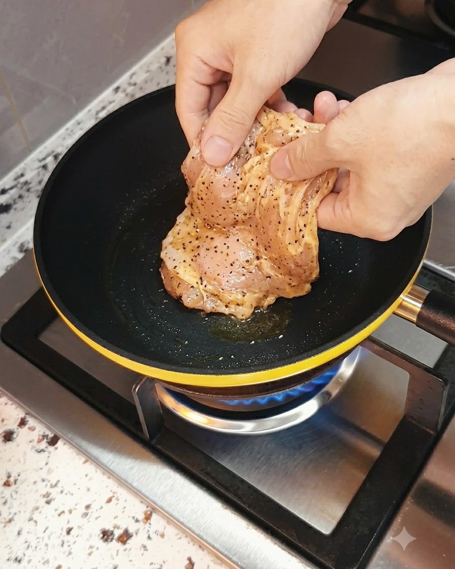ガス火が下にある熱したフライパンに入れられる、マリネされた鶏胸肉。