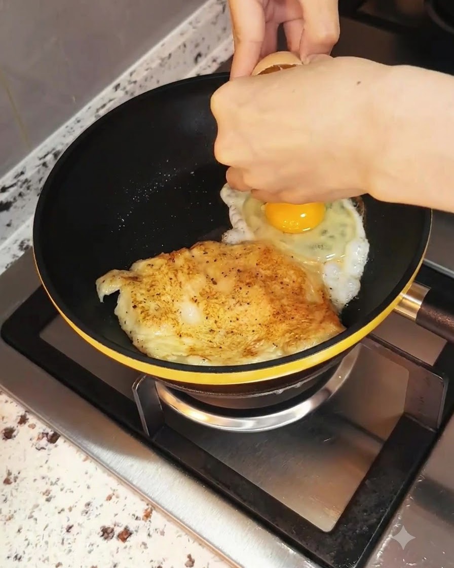 調理中の鶏胸肉の横にあるフライパンに割り入れられる卵。