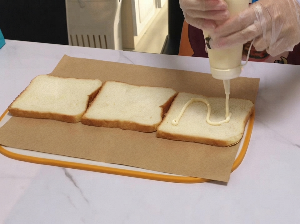 パーチメント紙の上の食パンに、ホワイトソースがジグザグ状に絞られている様子。