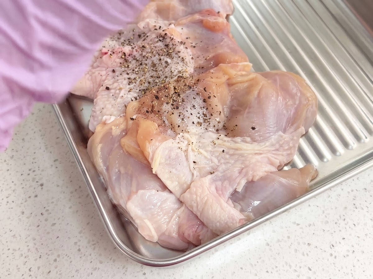 金属製トレイの中で挽きたて黒こしょうで味付けされた骨なし鶏もも肉。