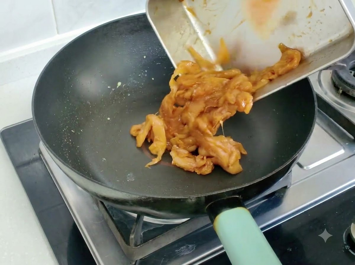 フライパンに移されて炒められているマリネ済みの鶏肉スライス。