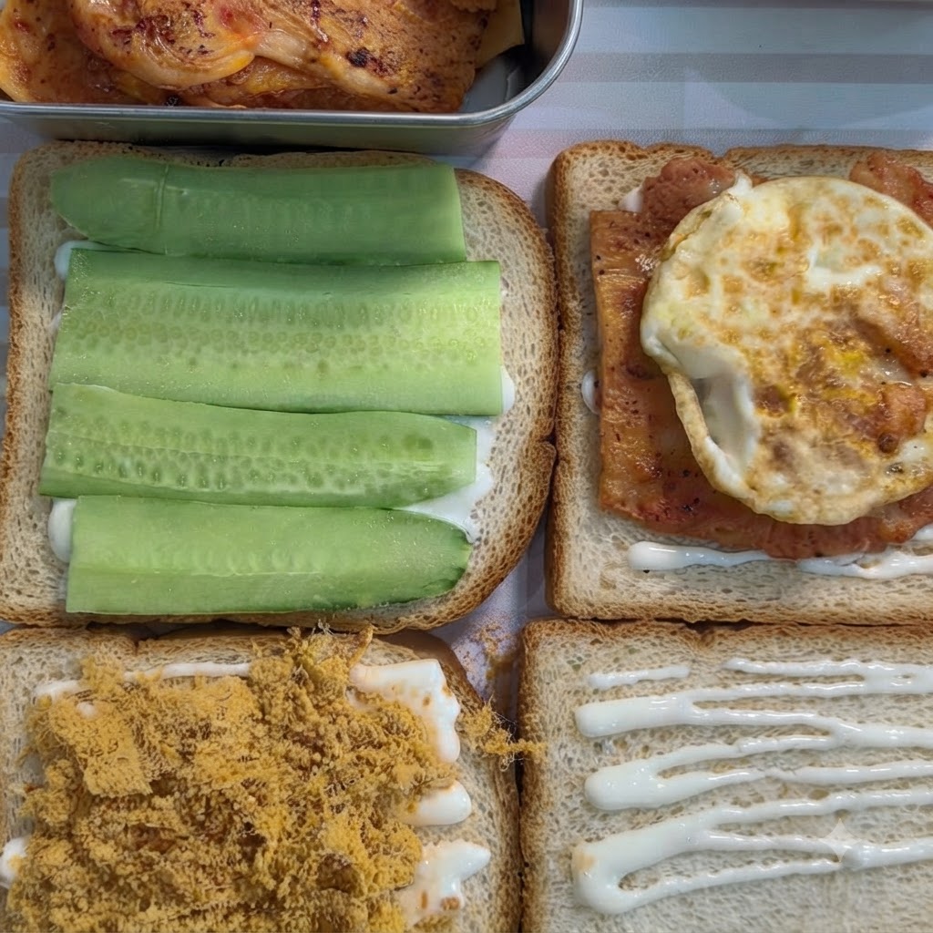 白いスプレッドが塗られた食パンの上に、調理された味付けチキンと目玉焼きが乗せられている様子。