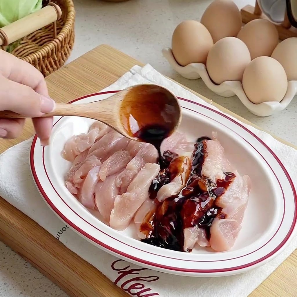白い皿に並べられた生の鶏肉の細切りに、木製のスプーンからソースが注がれている様子
