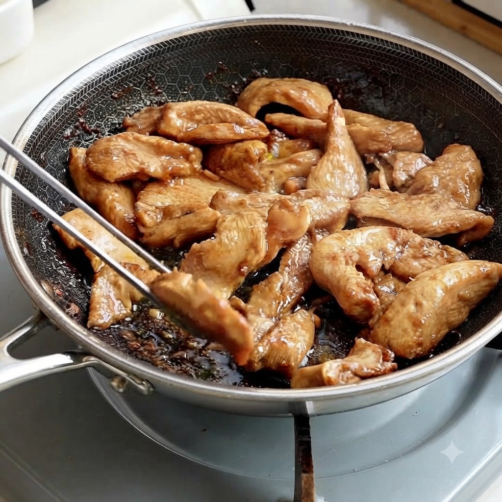 調理用トングで、フライパンから炒め上がった鶏肉の細切りを取り出している様子