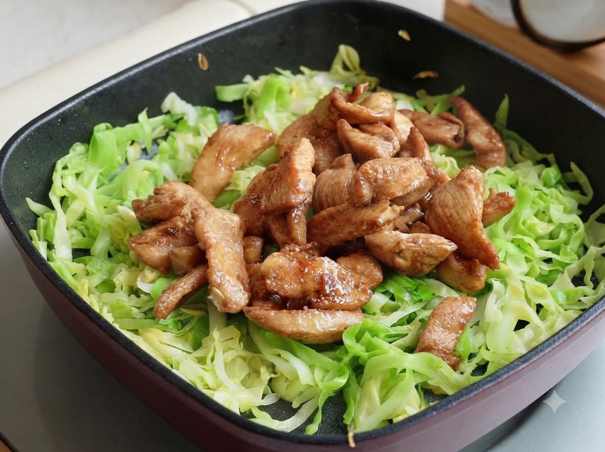 フライパンの千切りキャベツの上に、あらかじめ調理した鶏胸肉の細切りを乗せ、2つの山に分けている様子