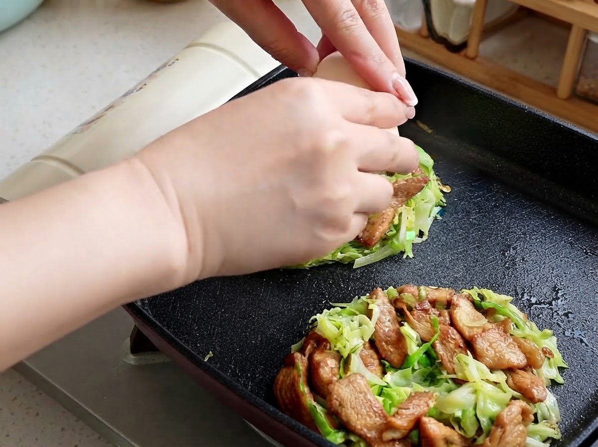 両手で生卵を割り、フライパンの中のキャベツとチキンの山の中心に落とし込んでいる様子