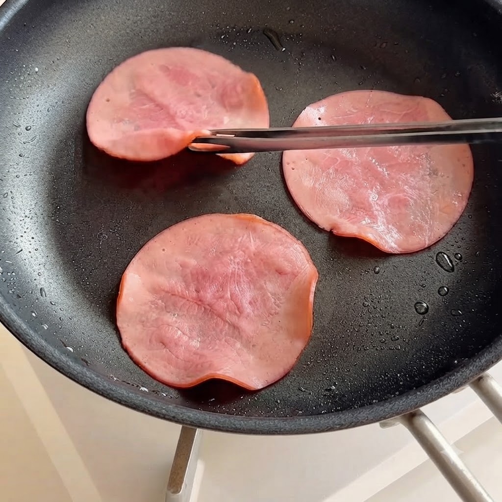 フライパンの中で箸を使って裏返されるハムのスライス。