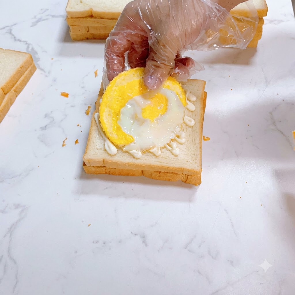 マヨネーズが塗られた白いパンの上に、目玉焼きが慎重に配置されているところ。