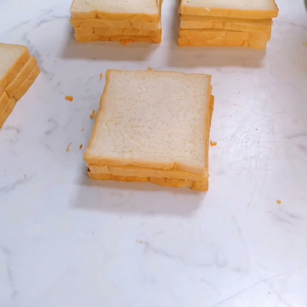 サンドイッチのスタックの上に、3枚目の正方形の白い食パンが乗せられているところ。