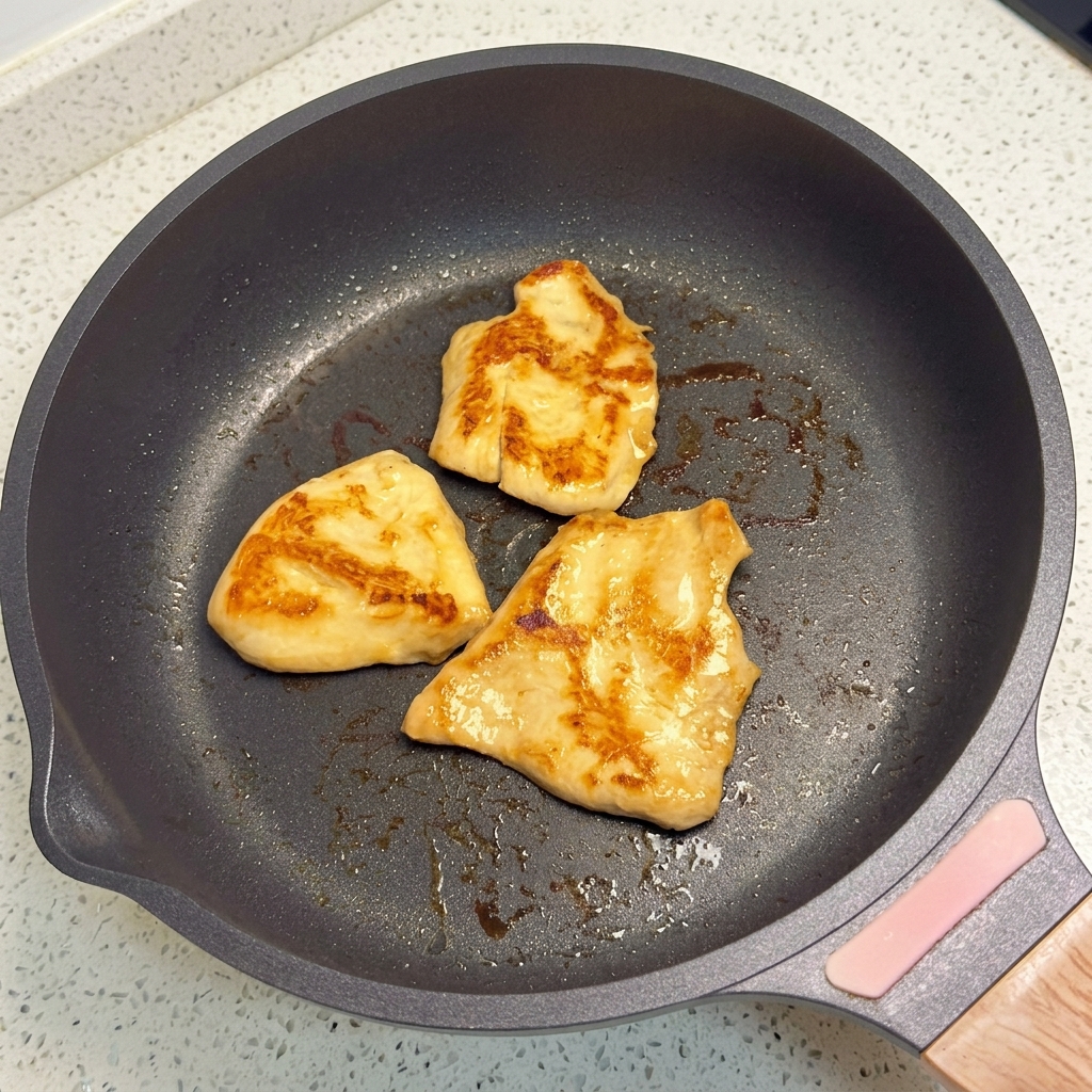 平底のフライパンできつね色になるまで焼かれている鶏肉のピース。