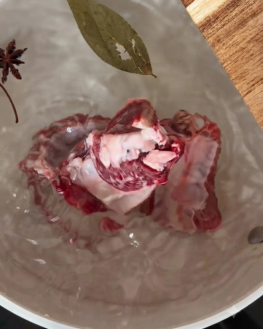 八角とローリエが浮いた水が入った鍋で煮込まれている豚スペアリブ