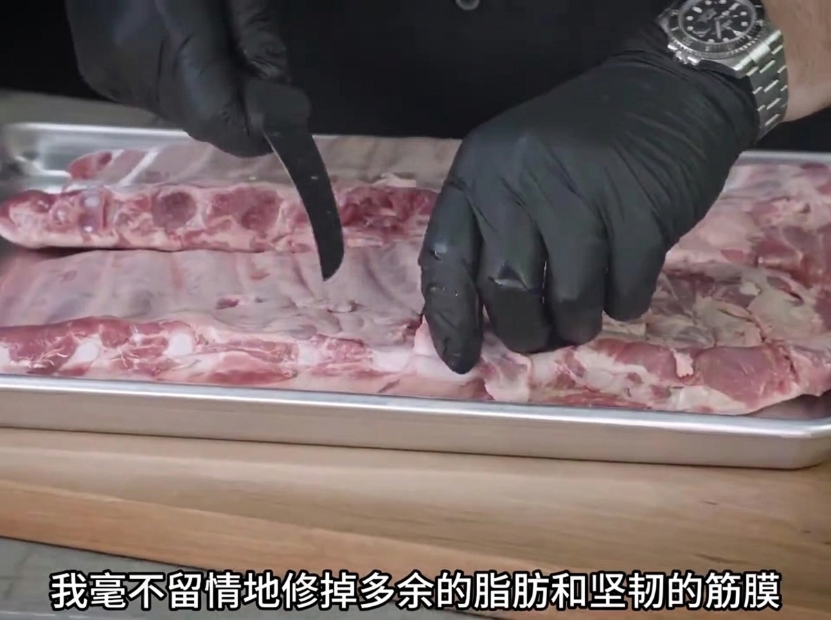 金属製のトレイの上で、手袋を着用した両手がナイフを使って生スペアリブの余分な脂を切り落としている様子。