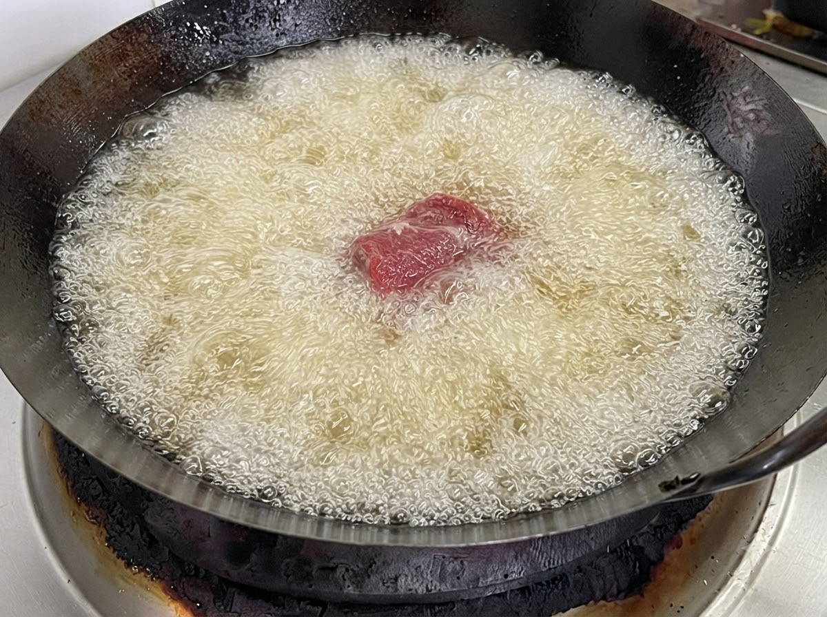 熱した揚げ油で泡立つ中華鍋の中に、1切れの豚スペアリブが投入されている様子。