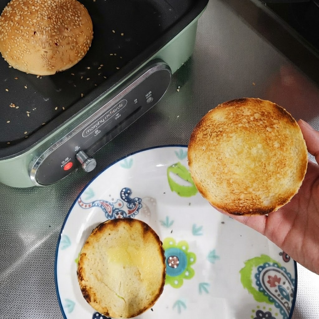 皿の上に置かれたトースト済みのバーガーバンズの半分と、パンの中でトーストされている丸ごとのバンズ。