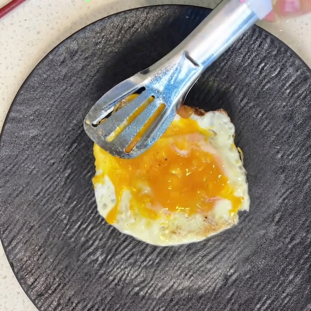トングを使ってスライストマトの上に目玉焼きを慎重にのせている様子。