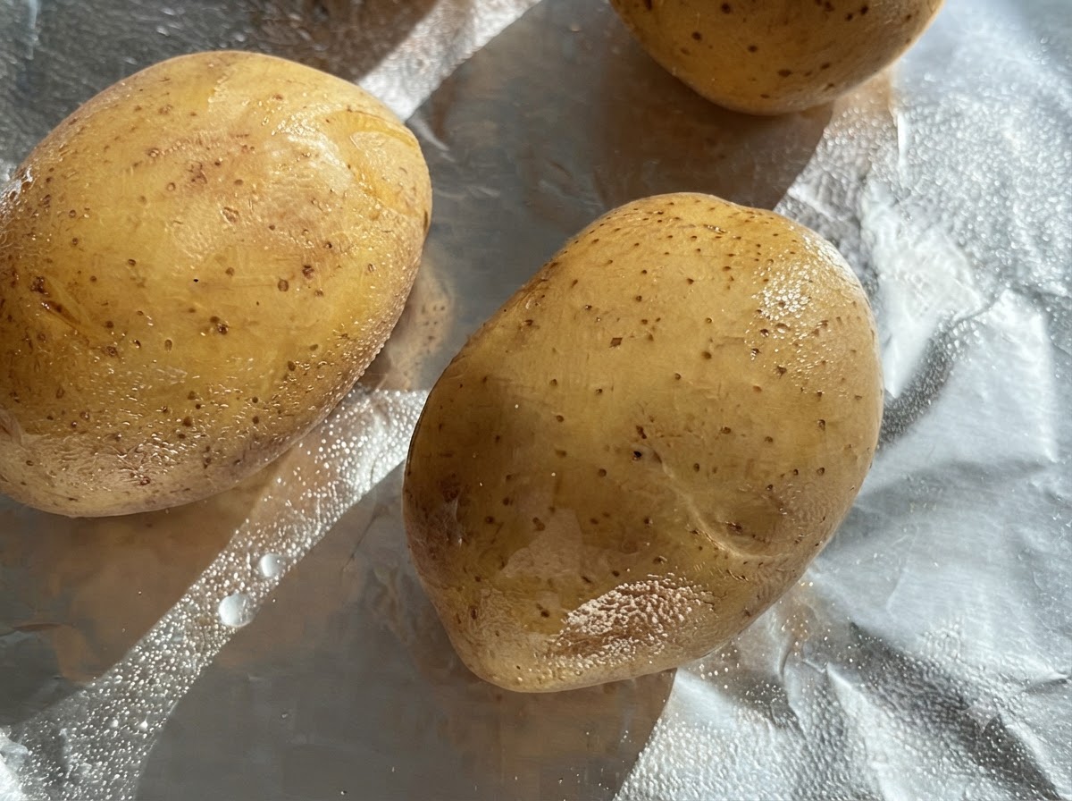 アルミホイルの上に置かれた、油を塗られた生の丸ごとのじゃがいも。