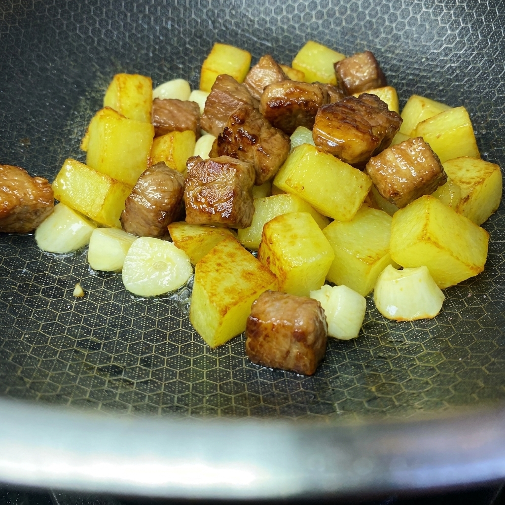 黄金色に揚がったポテトとソテーした豚肉が中華鍋の中で一緒合わされている様子