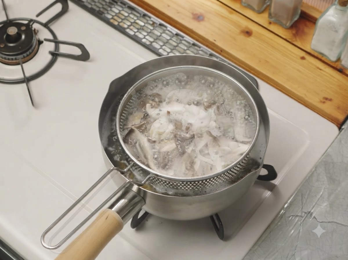 コンロ上の鍋に入れられたメッシュのストレーナーバスケットの中で、ちぎったキノコが茹でられている様子。