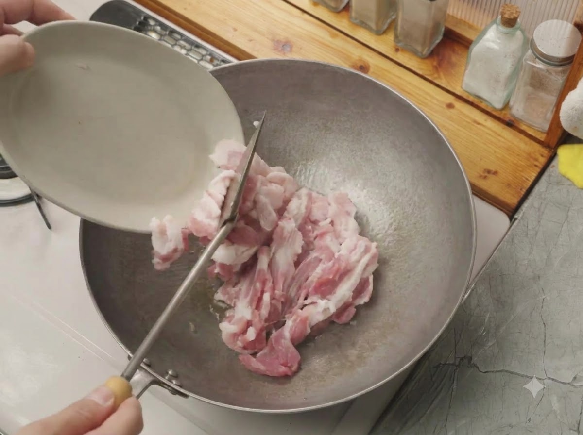 白い小皿から切った生の豚バラ肉が、熱した中華鍋に入れられている様子。