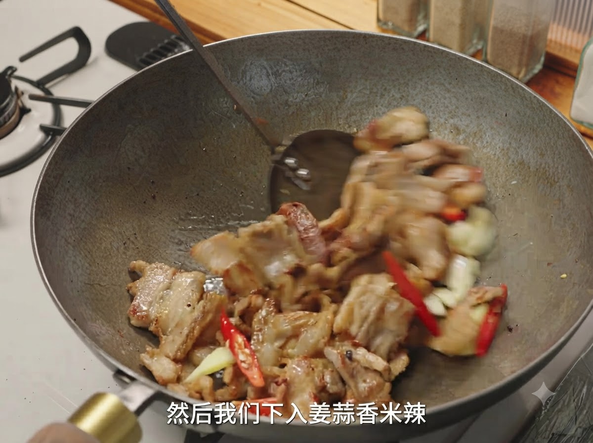 刻んだ生姜、ニンニク、赤唐辛子が、中華鍋で香ばしく炒められた豚肉と一緒に混ぜ合わせられている様子。