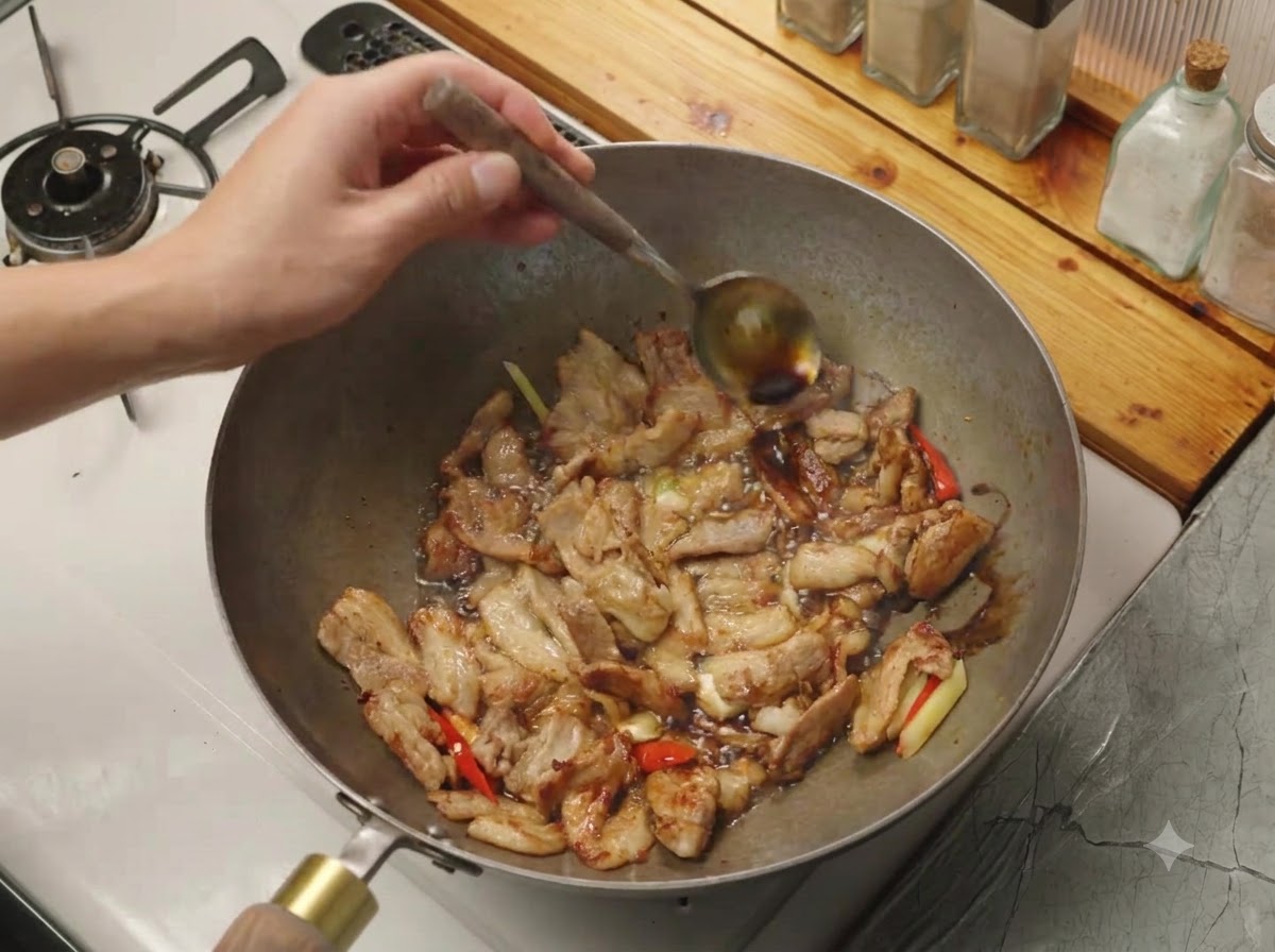 肉と香味野菜が入った中華鍋の熱い縁に沿って、スプーンから醤油が注がれている様子。