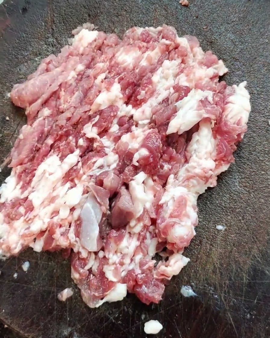 木のまな板の上で、刻んだ豚肩ロース肉の塊と包丁が置かれている様子。